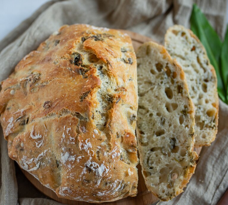 Bärlauchbrot mit Nüssen auf einem Geschirrtuch, daneben ein paar Bärlauchblätter. | © Getty Images/ A_Lein