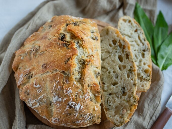 Bärlauchbrot mit Nüssen auf einem Geschirrtuch, daneben ein paar Bärlauchblätter. | © Getty Images/ A_Lein