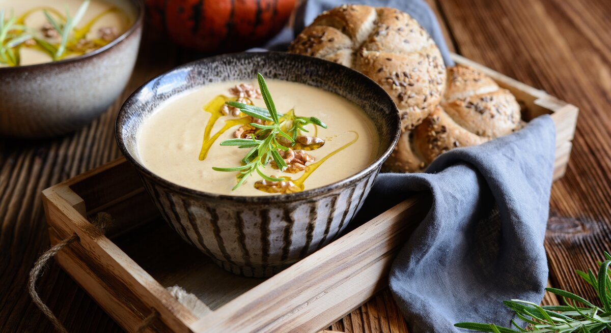 Eine Schüssel mit Walnuss-Kürbissuppe auf einem Holztablett.