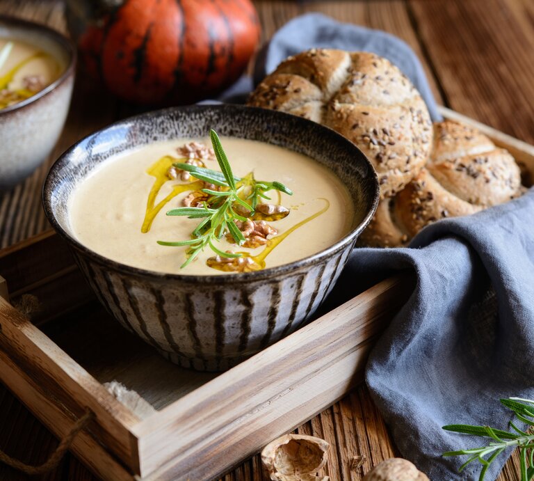 Eine Schüssel mit Walnuss-Kürbissuppe auf einem Holztablett. | © GettyImages/NoirChocolate