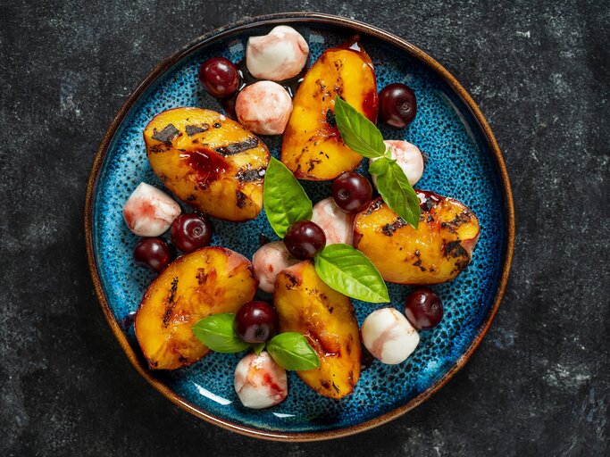Draufsicht: Dunkler Untergrund, eine Mozzarella-Pfirsichsalat auf einem rustikalem blau-schwarzen Teller, | © Shutterstock / OlegD