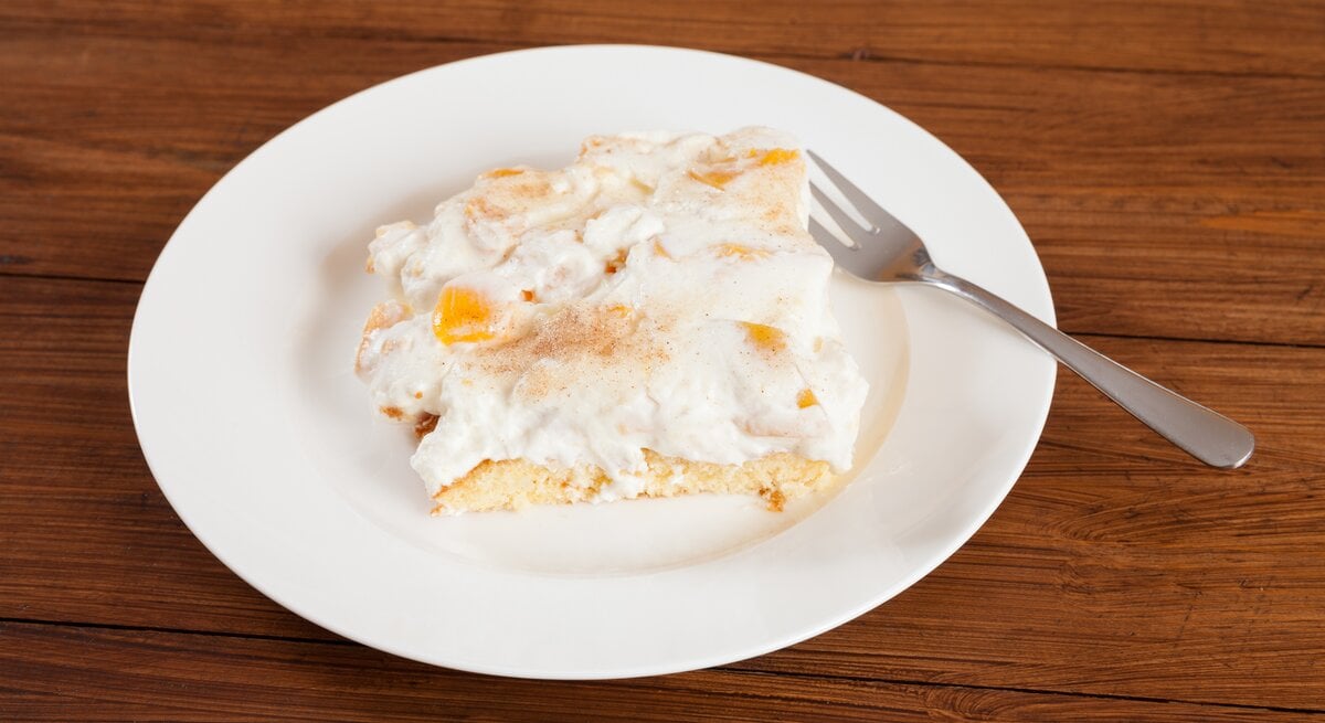 Ein angeschnittenes Stück Pfirsich-Schmand-Kuchen auf weißem Teller. 