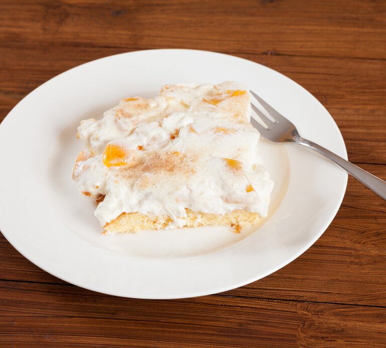 Ein angeschnittenes Stück Pfirsich-Schmand-Kuchen auf weißem Teller.  | © iStock/Tuned_In