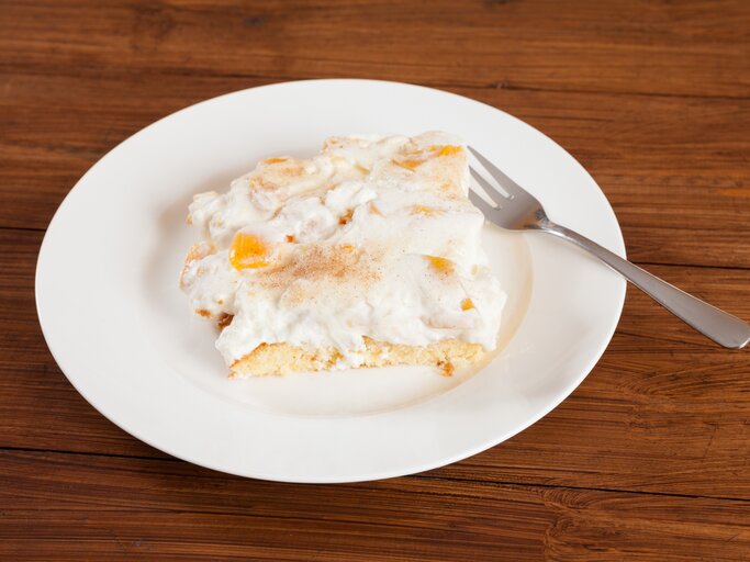 Ein angeschnittenes Stück Pfirsich-Schmand-Kuchen auf weißem Teller.  | © iStock/Tuned_In