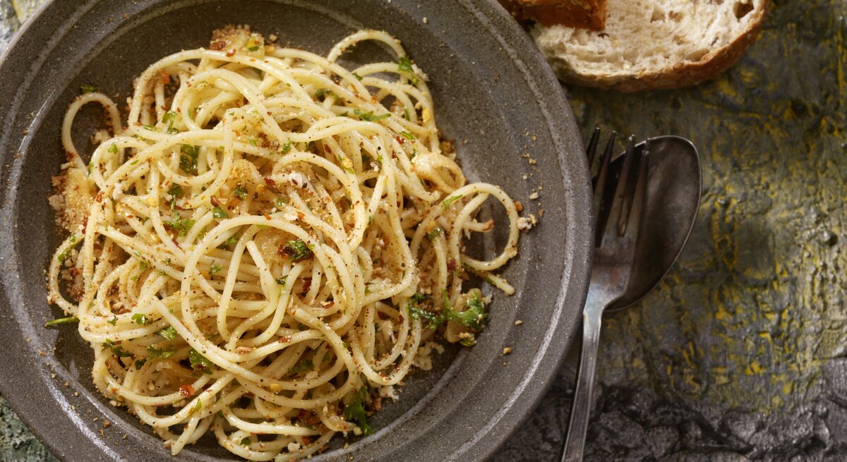 Draufsicht auf einen dunklen Teller befüllt mit Spaghetti Aglio, Olio e Peperoncini. 