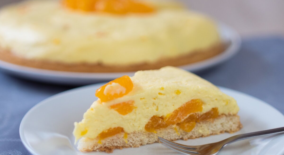 Ein angeschnittenes Stück Schüttelkuchen mit Mandarinen auf einem weißen Teller. 