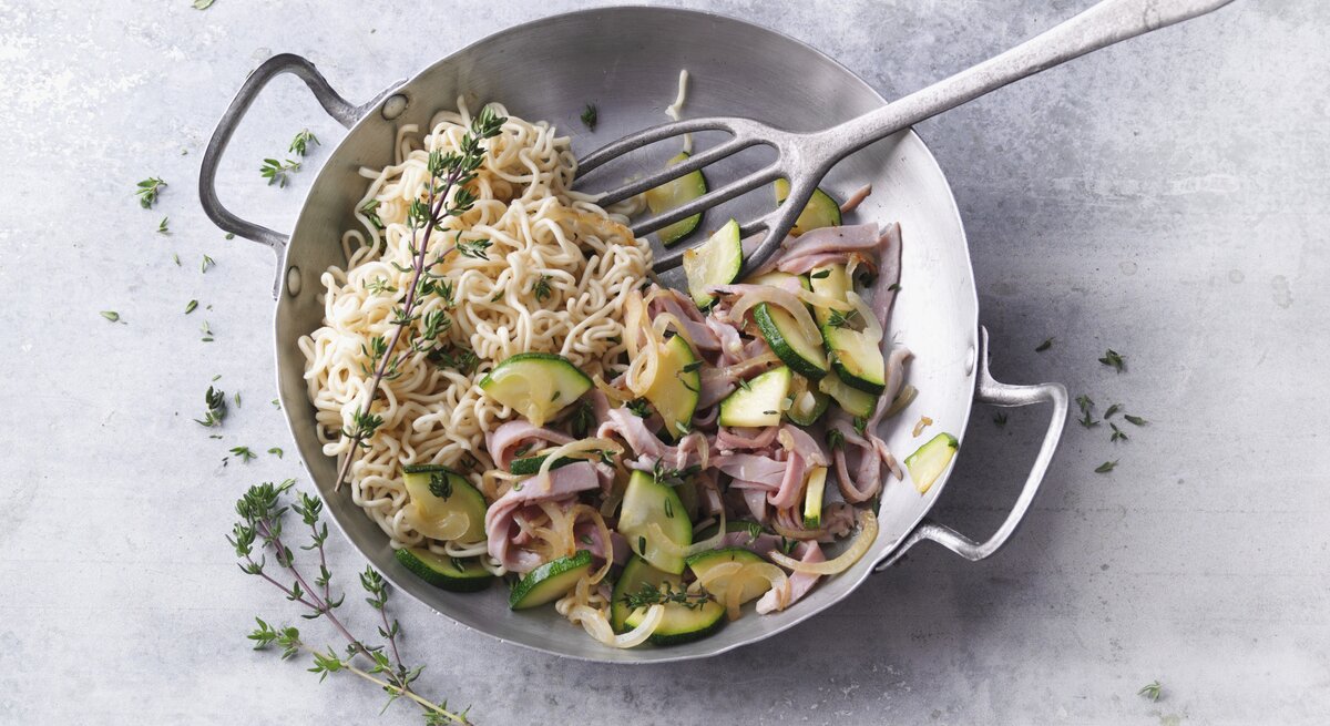 Ein silberner Wok mit dem Gericht auf einem grauen Steintisch direkt von oben fotografiert.