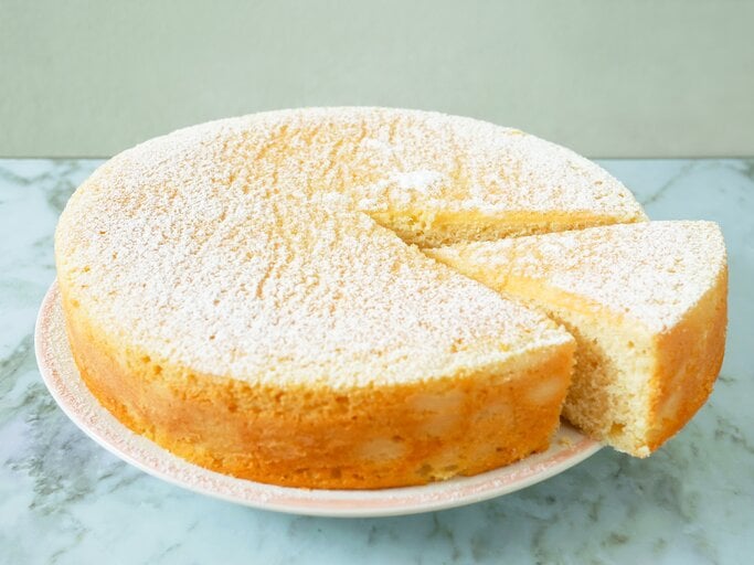 Runder, heller, angeschnittener Kuchen auf weißem Teller, bestäubt mit Puderzucker.  | © iStock.com/p_saranya