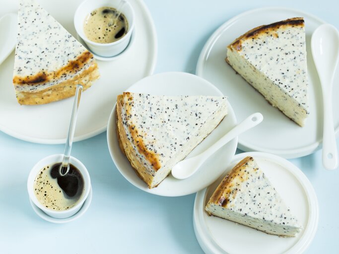 Mehrere Stücken vom Käsekuchen auf weißem Geschirr und einer hellblauen Tischdecke. Daneben noch Kaffee in kleinen Tassen. Alles direkt von oben fotografiert. | © StockFood / Gräfe & Unzer Verlag / D'Angelo, Vivi