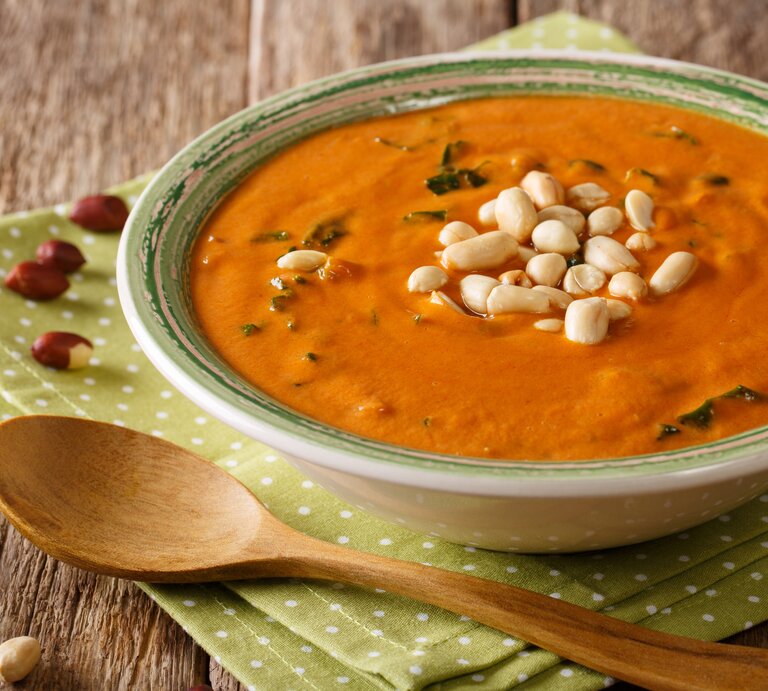 Seitliche Ansicht auf eine Schüssel afrikanische Erdnusssuppe auf Holztisch. | © iStock/ALLEKO