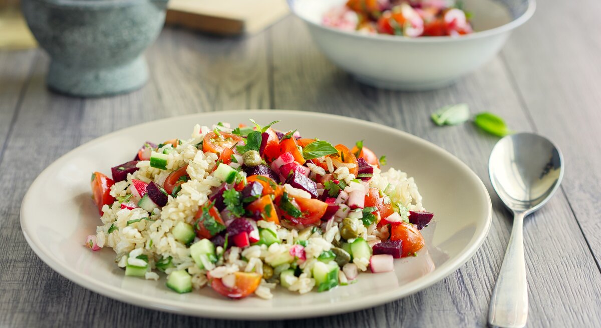 Ein Teller Reissalat mit Curry-Joghurt-Dressing auf einem Untergrund aus Holz / Frontalsicht