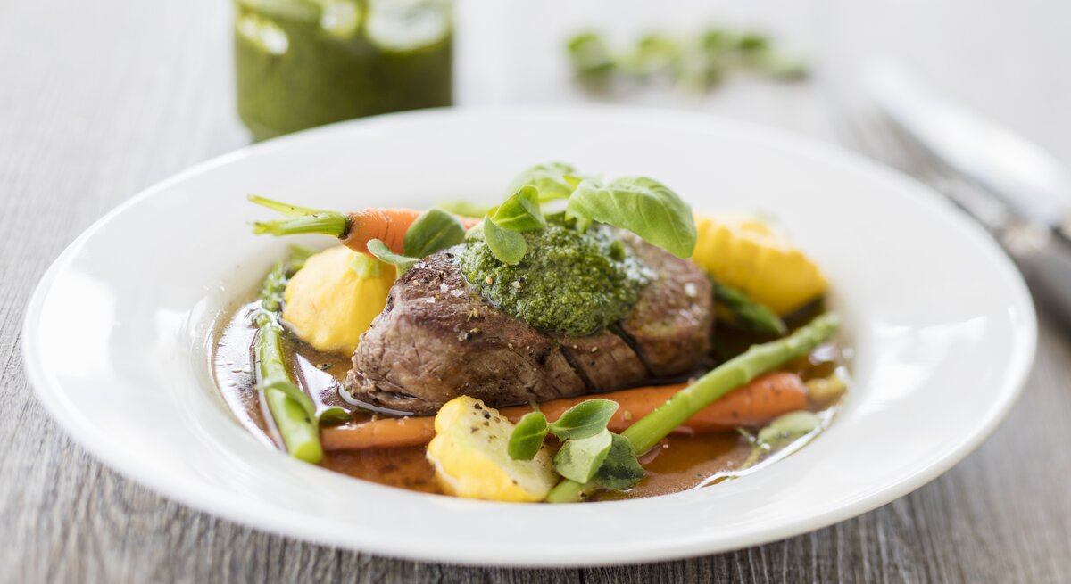 Das Rinderfilet auf einem weißen Teller mit reichlich Gemüse vor weißem Hintergrund.