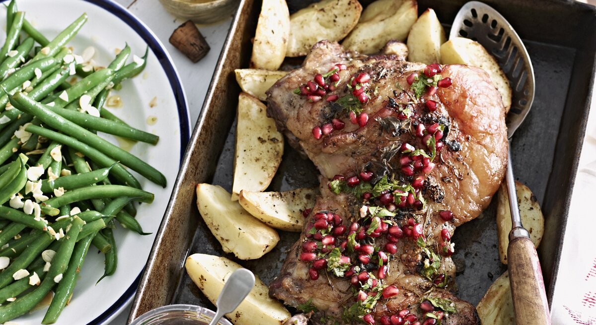 Lammbraten mit Granatapfelkernen und Gemüse. Alles auf einem Tisch arrangiert und von oben fotografiert.