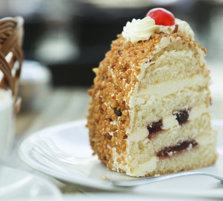 Ein Stück vom Frankfurter Kranz auf einem weißen Teller nah und von der Seite fotografiert. | © iStock/Mariha-kitchen