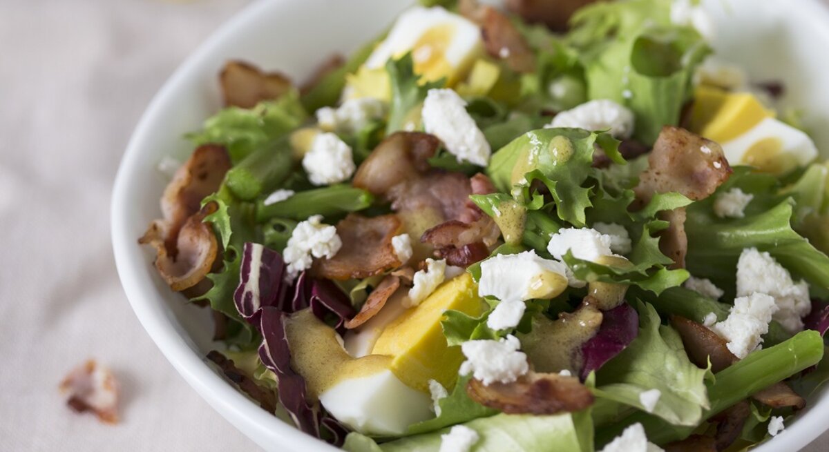 Spargelsalat mit Ei, Speck und Feta auf einem Teller.