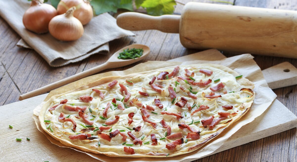 Frisch gebackener Flammkuchen mit Speck auf einem Holzbrett.