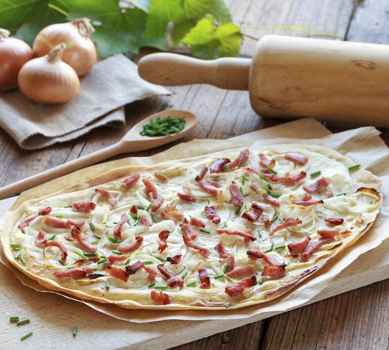 Frisch gebackener Flammkuchen mit Speck auf einem Holzbrett. | © istock/juefraphoto