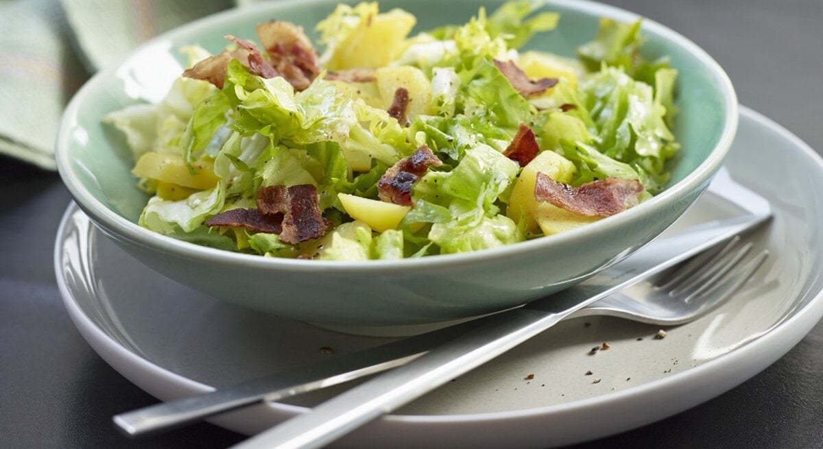 Endiviensalat mit Kartoffeln und Speck  im tiefen Teller mit hohem Rand / Nahaufnahme / Frontal