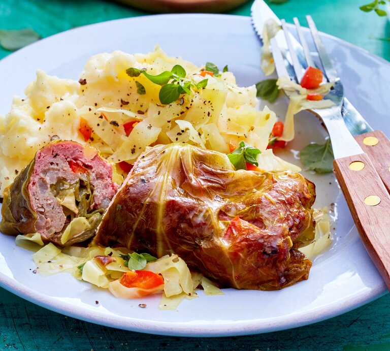 Spitzkohl-Rouladen an Kartoffelpüree auf einem weißen Teller und blauem Untergrund. Alles von schräg oben fotografiert. | © Isabell Triemer