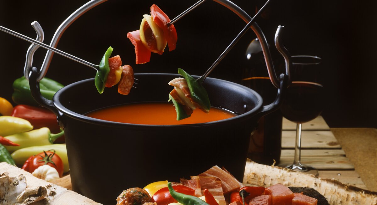 Eine Nahaufnahme eines Topfes mit Tomaten-Fondue, umgeben von Zutaten und einem Glas Rotwein. 