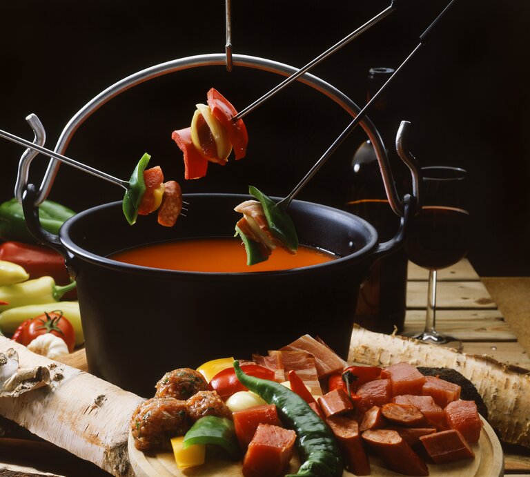 Eine Nahaufnahme eines Topfes mit Tomaten-Fondue, umgeben von Zutaten und einem Glas Rotwein.  | © StockFood / Bischof, Harry