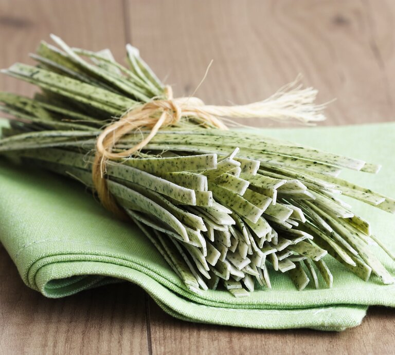 Ein Bündel ungekochte, selbst gemachte Bärlauchnudeln auf einem grünen Tuch, das wiederum auf einem Holztisch liegt.  | © iStock/TeQui0