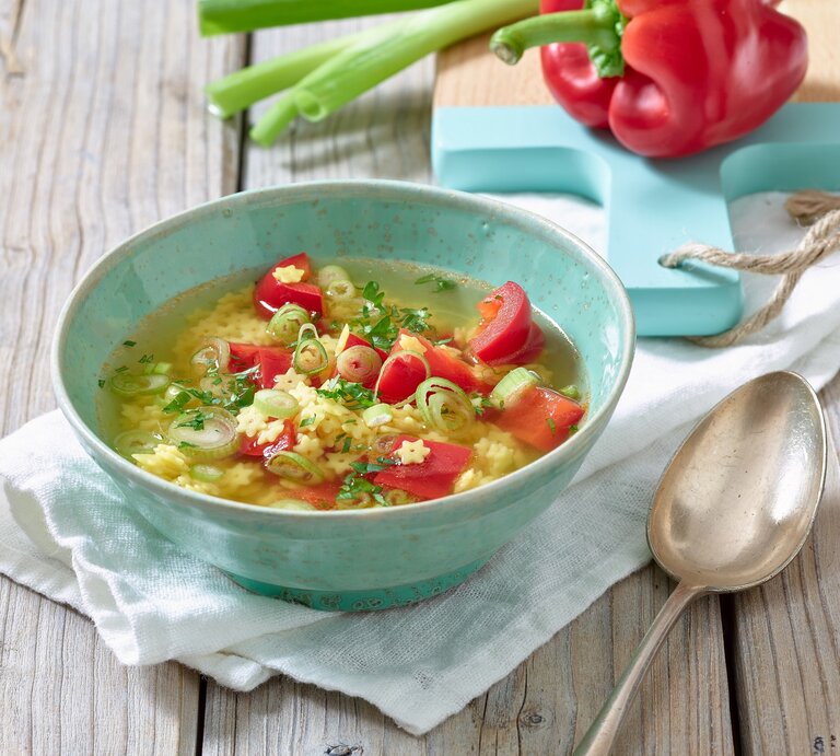 Eine dampfende Schüssel klare Nudelsuppe mit roten Paprikawürfeln, grünen Lauchzwiebelringen und Sternchennudeln. | © Matthias Liebich