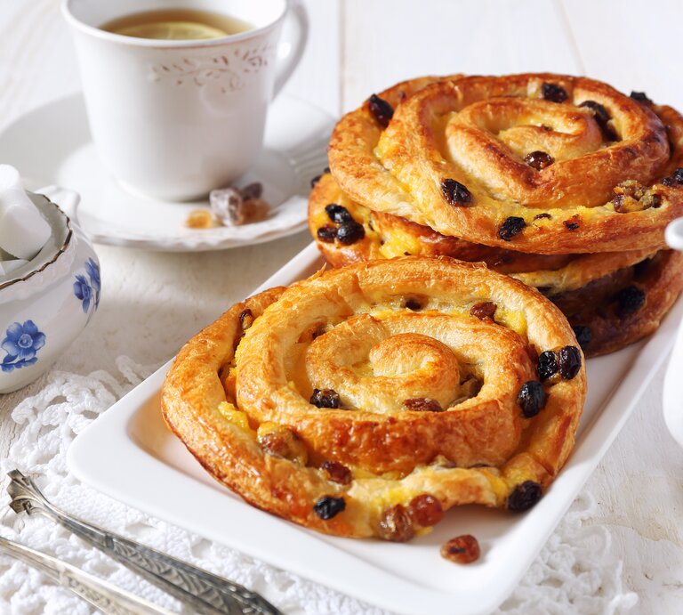 Mehrere runde Gebäckstücke mit Rosinen auf einem langen, eckigen Teller. | © iStock/Yulia Vinogradova