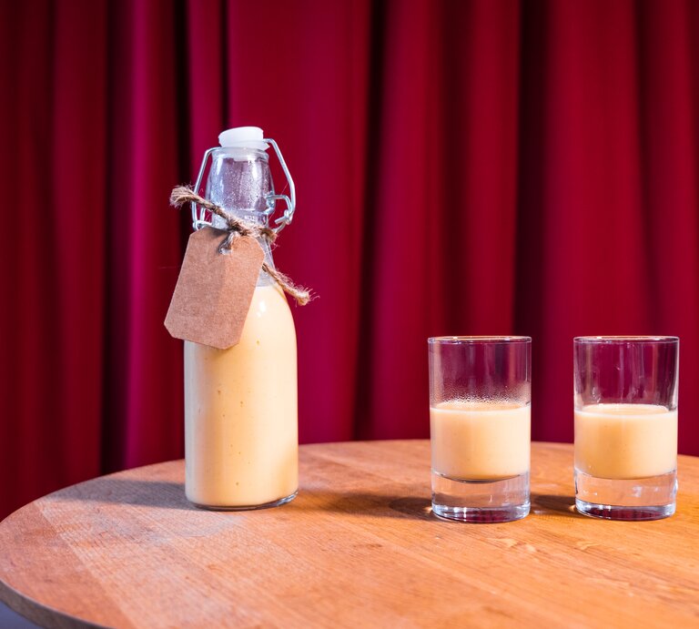 zwei Gläschen Eierlikör, daneben eine kleine Flasche. Das Ganze steht auf einem Holztisch, dahinter ein roter Vorhang. | © BILD der FRAU/Pako Cardenas Quijada