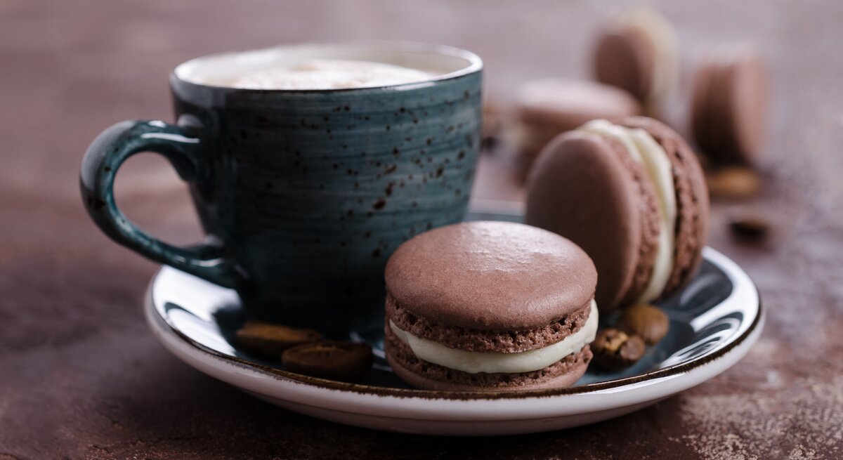 Süße Tiramisu-Kekse auf blauem Teller mit Kaffeetasse vor braunem Hintergrund