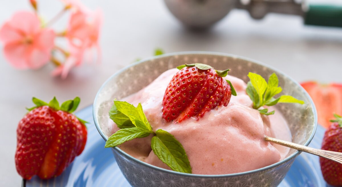 Erdbeer-Sahne-Sorbet in rundem Becher / Minzblättchen und eine Erdbeere als Deko / kleiner Löffel / Draufsicht / Nahaufname