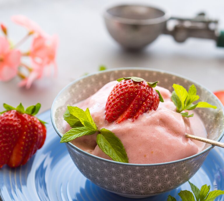 Erdbeer-Sahne-Sorbet in rundem Becher / Minzblättchen und eine Erdbeere als Deko / kleiner Löffel / Draufsicht / Nahaufname | © iStock/tenkende
