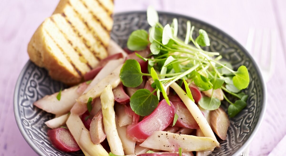 Eine Schale mit dem Salat auf einem fliederfarbenen Holztisch. Alles von schräg oben fotografiert.
