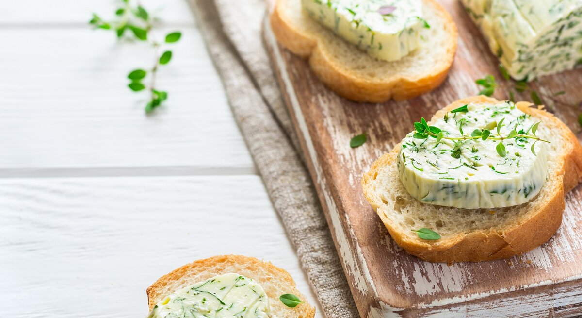 Ein paar Baguette-Scheiben mit Limetten-Koriander-Butter und Kräutern verziert auf einem Brett.