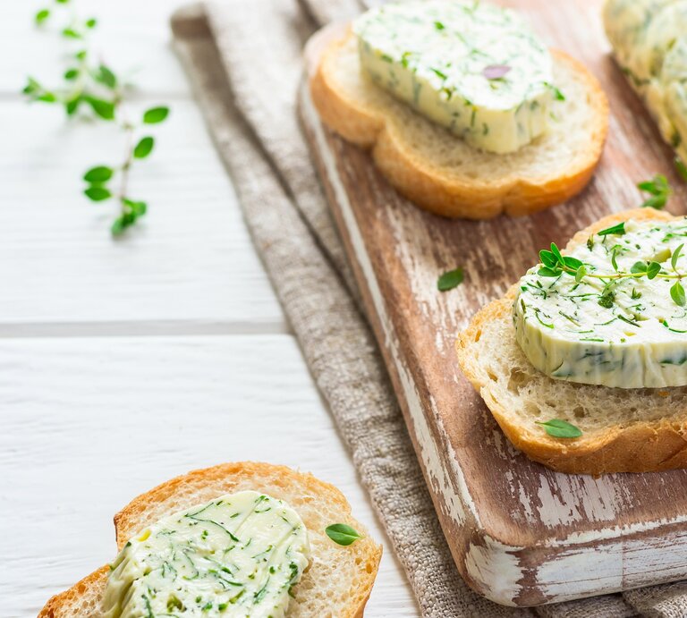 Ein paar Baguette-Scheiben mit Limetten-Koriander-Butter und Kräutern verziert auf einem Brett. | © Adobe Stock/ colnihko