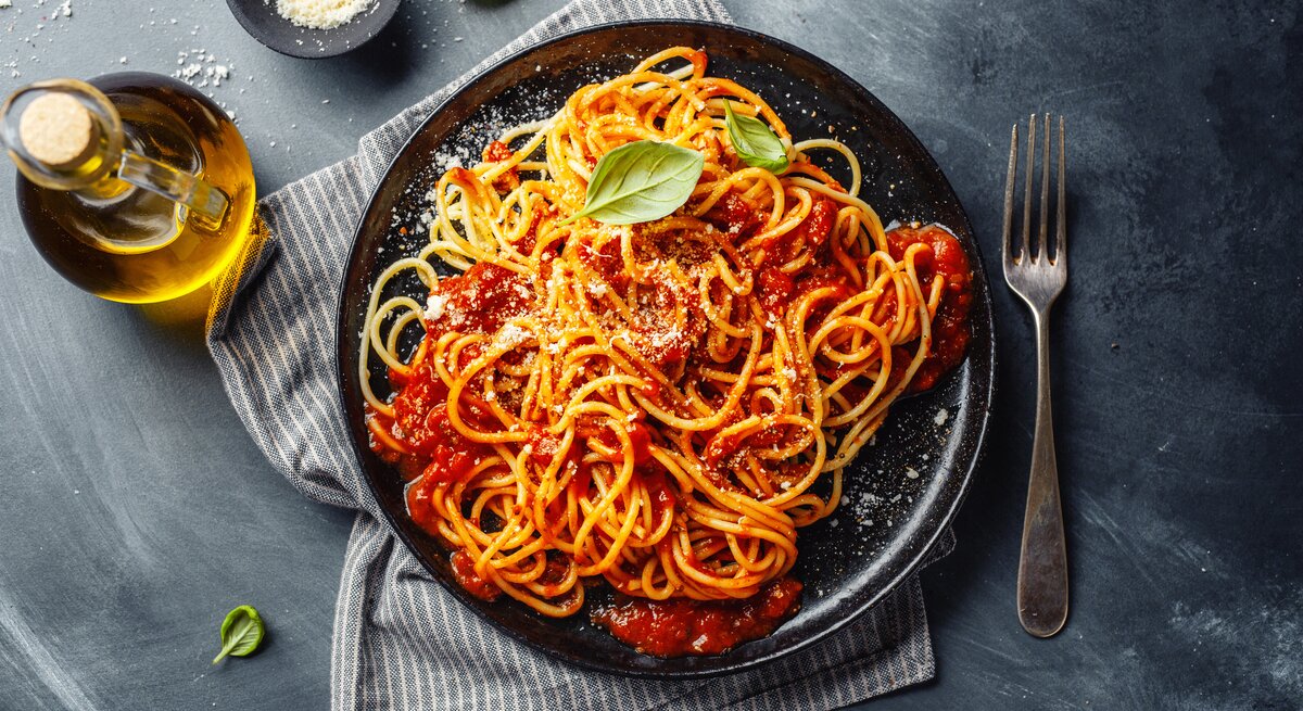 Eine PortiVegane Spaghetti Bolognese / frische Basilikumblätter / runder Teller / Gabel / geriebener Parmesan  / Kleine Flasche mit Öl / Küchentuch /