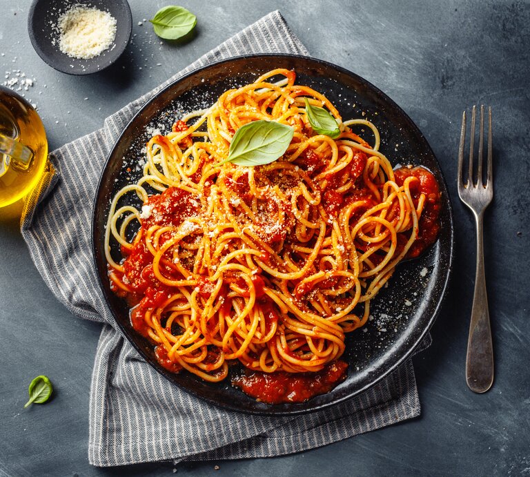 Eine PortiVegane Spaghetti Bolognese / frische Basilikumblätter / runder Teller / Gabel / geriebener Parmesan  / Kleine Flasche mit Öl / Küchentuch / | © Getty Images / nerudol