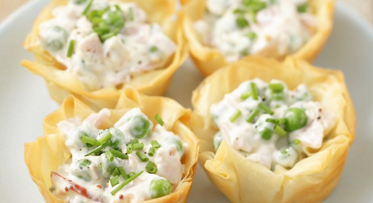 Vier Filoteig mit Schinken, Erbsen und Mayonnaise gefüllt und mit Schnittlauch bestreut / Draufsicht, schräg