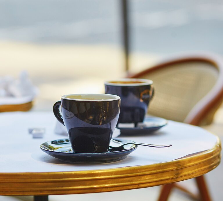 Frontalblick: Zwei French Hot Coffee in Tassen stehen auf einem runden Bistrotisch. An dem Tisch steht ein Stuhl. | © Shutterstock / Ekaterina Pokrovsky