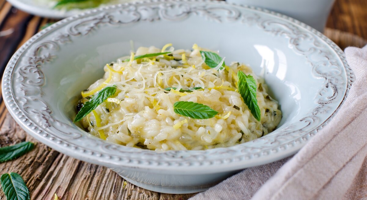 Ein tiefer Pasta-Teller mit Risotto mit Zitrone und Minze auf einem Holztisch.