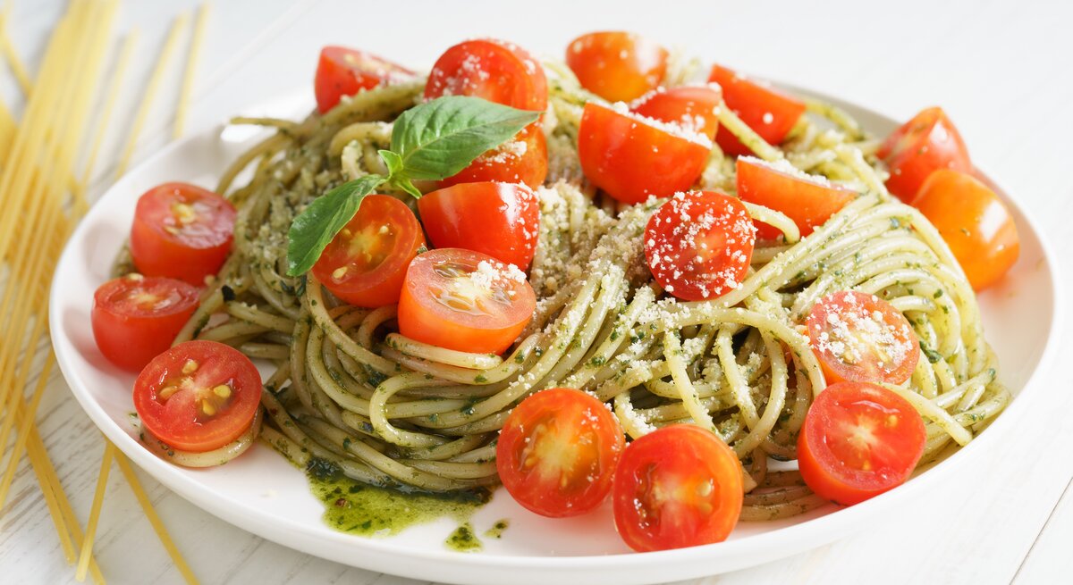 Pesto-Spaghetti-Salat mit Tomaten auf weißem Teller.