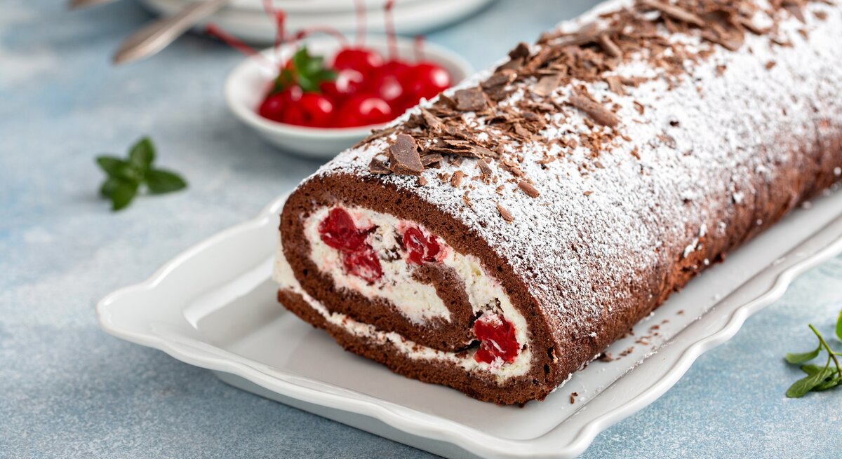 Draufsicht, schräg: Einen perfekten Biskuit, als cremige Rolle mit Sahne, Schokolade und Kirschen.