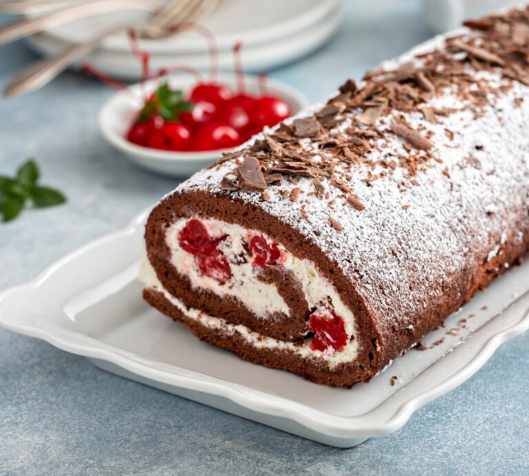Draufsicht, schräg: Einen perfekten Biskuit, als cremige Rolle mit Sahne, Schokolade und Kirschen. | © Getty Images / 	VeselovaElena