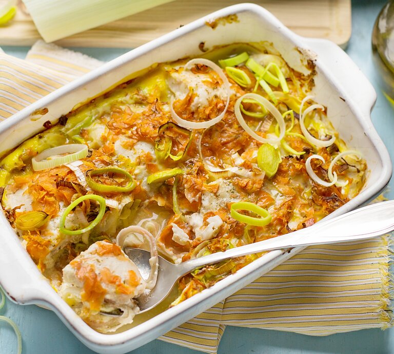 Ofengericht in weißer Auflaufform mit Fisch, Möhren und Lauch. Daneben Salzstreuer, eine Kanne Öl und ein Geschirrtuch. | © Getty Images/ larik_malasha