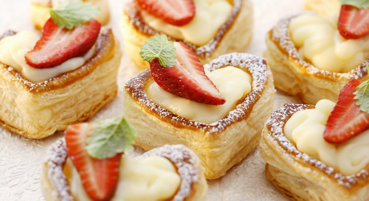 Draufsicht schräg: mehrere Vanillepudding im Blätterteigherz mit Erdbeeren.