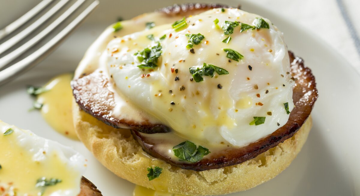 Seitliche Ansicht eines Brötchens mit pochiertem Ei und Sauce hollandaise. 