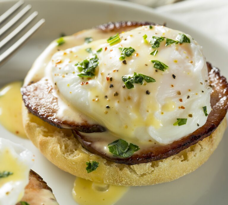 Seitliche Ansicht eines Brötchens mit pochiertem Ei und Sauce hollandaise.  | © iStock/bhofack2