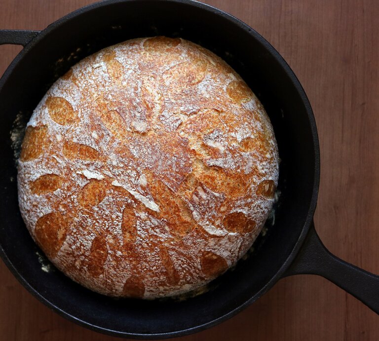 Knuspriges Topfbrot in einem Gusseisentopf. Der Topf steht auf einem braunen hölzernen Untergrund.  | © GettyImages/Katrin Ray Shumakov