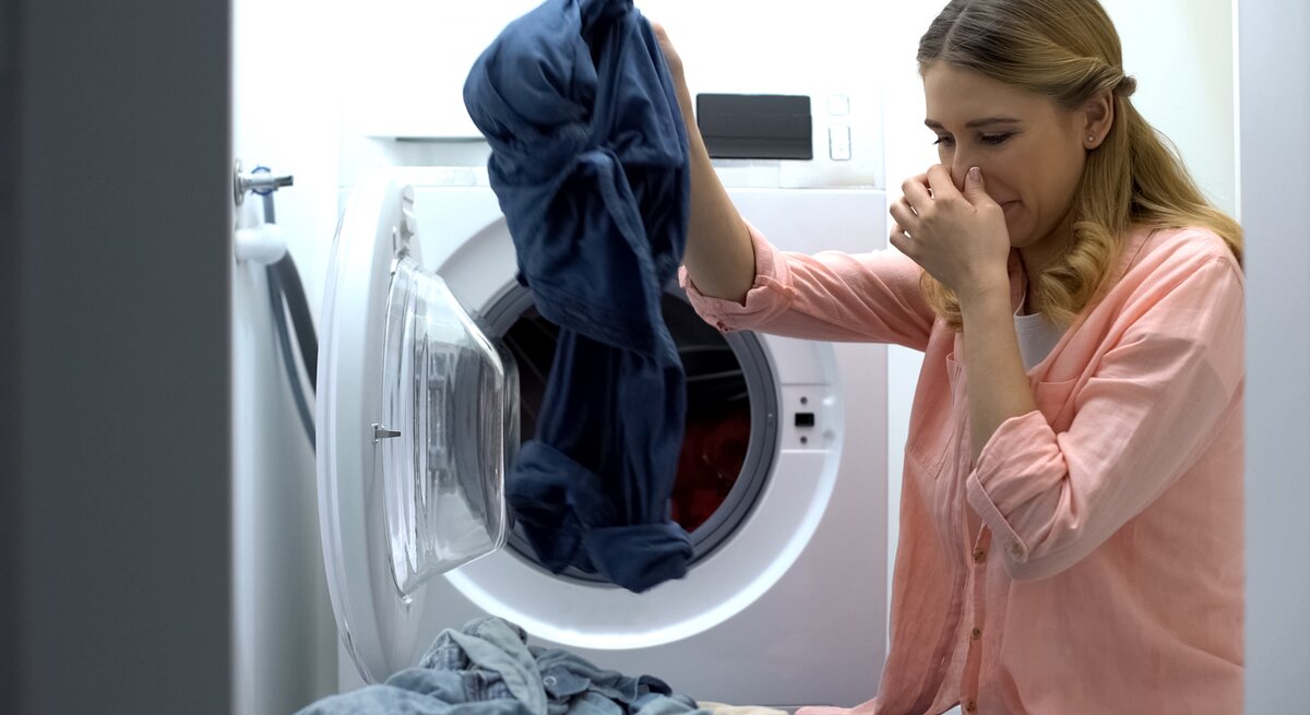 Frau holt mit der einen Hand Wäsche aus der Waschmaschine und hält sich mit der anderen die Nase zu