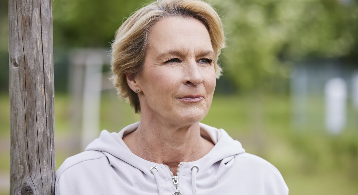 Martina Voss-Tecklenburg steht in einem Park und schaut zur Seite.